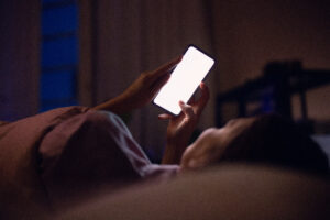 Person doom scrolling on her phone in bed at night