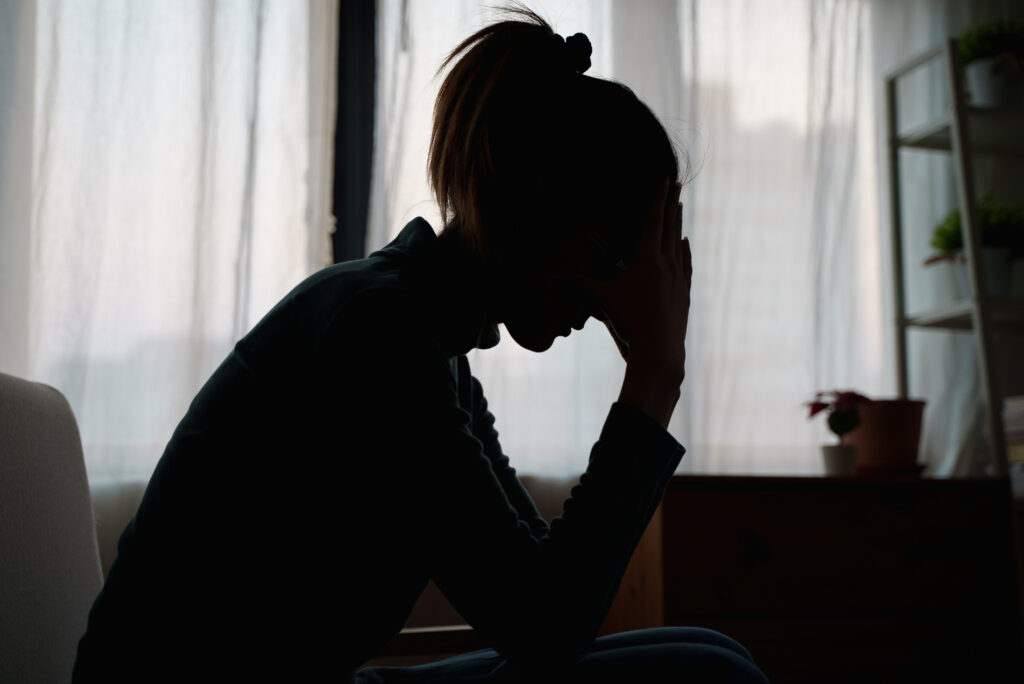 A silhouette of a seated woman leaning forward with her head in her hands.
