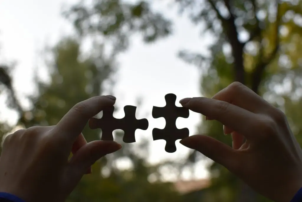 An outdoor scene of two hands holding puzzle pieces near each other.