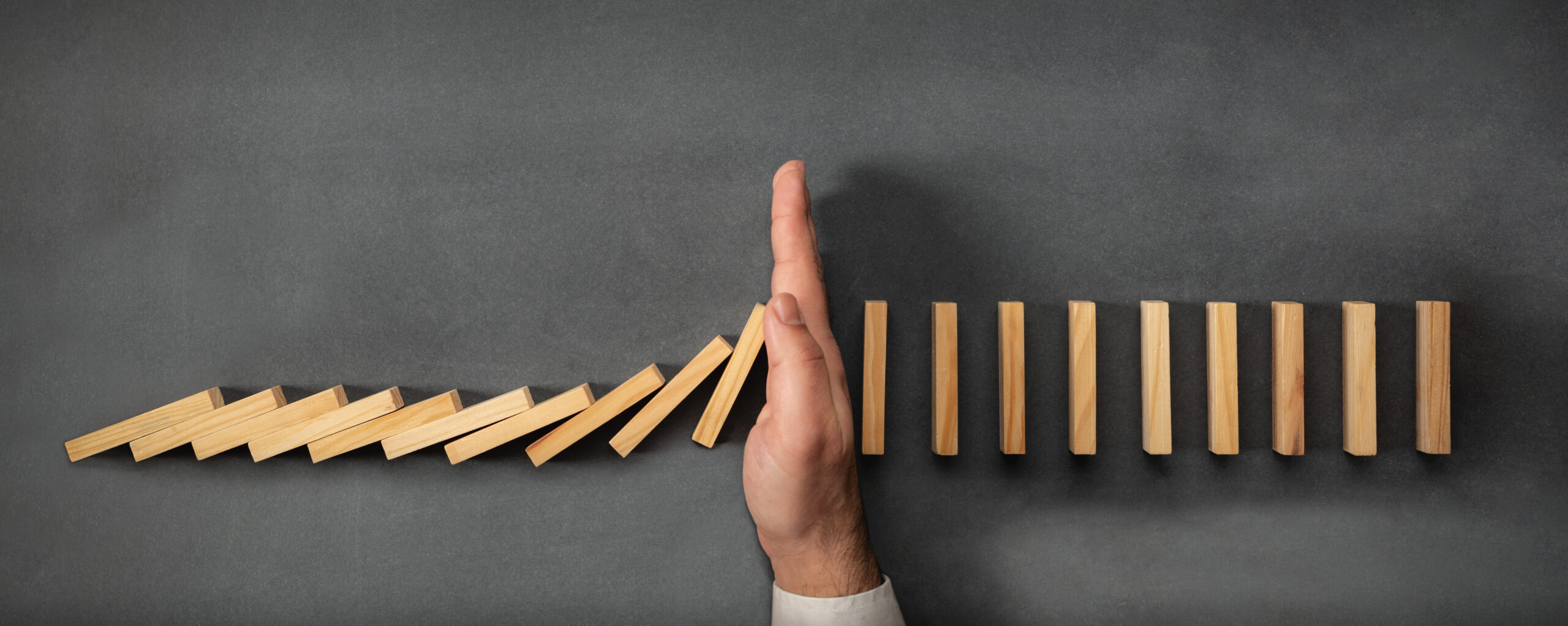 A woman blocks a row of falling dominoes with her hand, preventing any more from falling over.