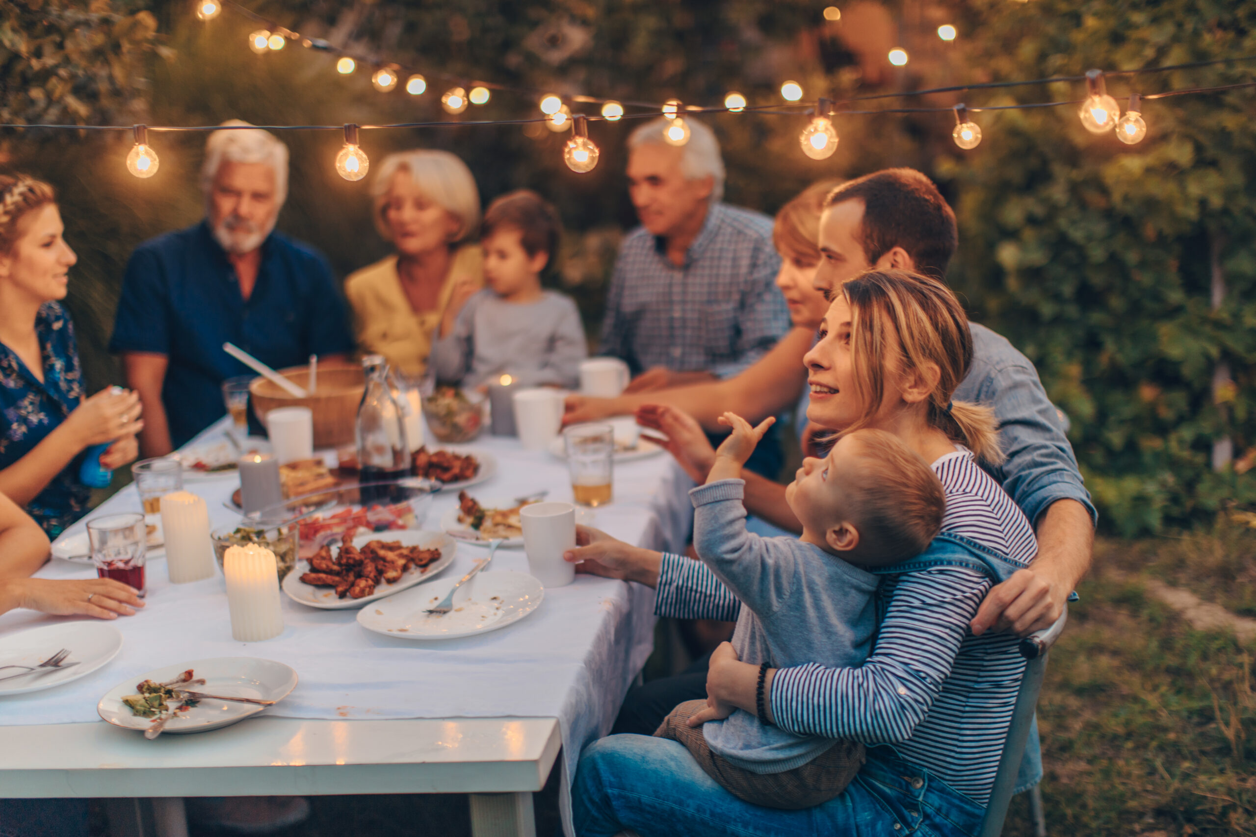 A big family gathers for dinner outside under string lights.